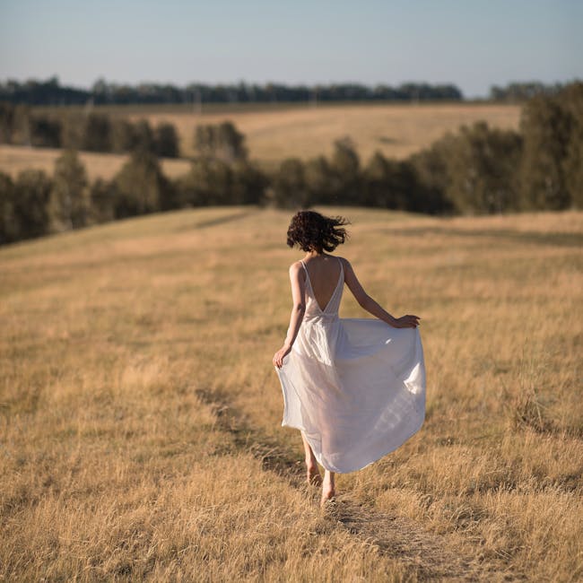 A woman with long hair in a white dress walking through a sunny meadow, capturing a serene moment.